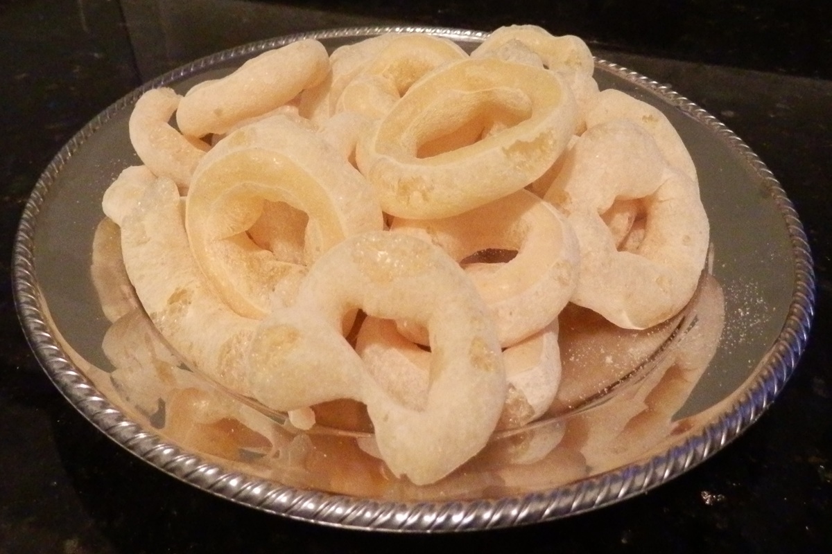 Biscoitos de polvilho assados dourados em formato de argola sobre pano de prato branco com xícara de café ao fundo
